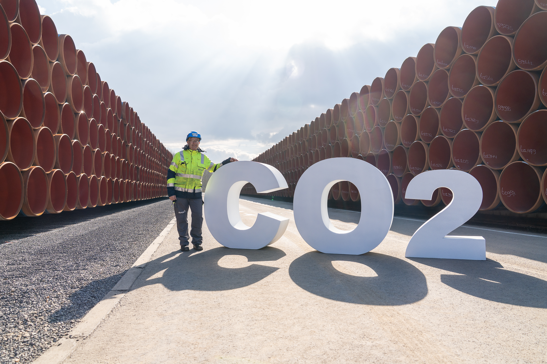 Employee with Fluxys CO2 sign next to pipelines.